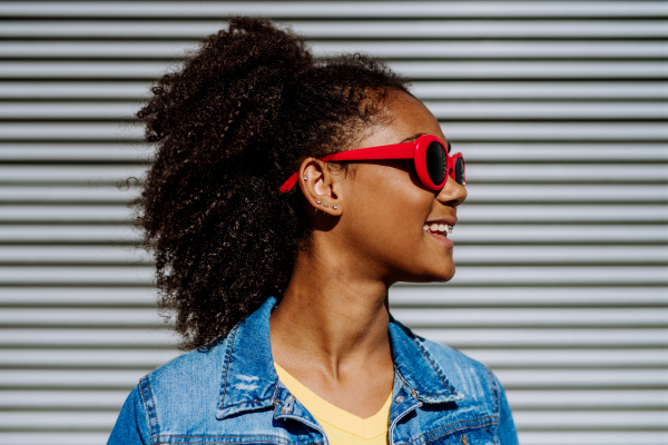 Portrait of young happy multiracial teenage girl with red sunglasses and afro hairstyle, standing outdoor.