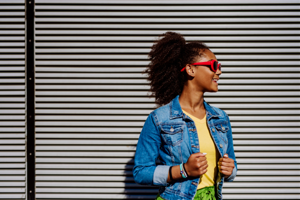 Portrait of young happy multiracial teenage girl with red sunglasses and afro hairstyle, standing outdoor.