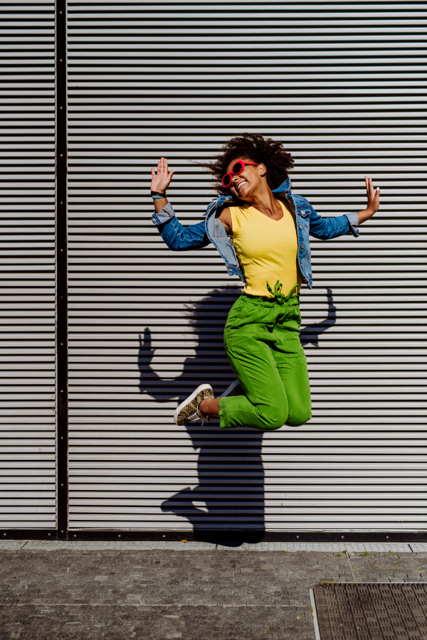 Young happy multiracial teenage girl with red sunglasses and afro hairstyle, jumping and posing outdoor.