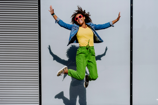 Young happy multiracial teenage girl with red sunglasses and afro hairstyle, jumping and posing outdoor.