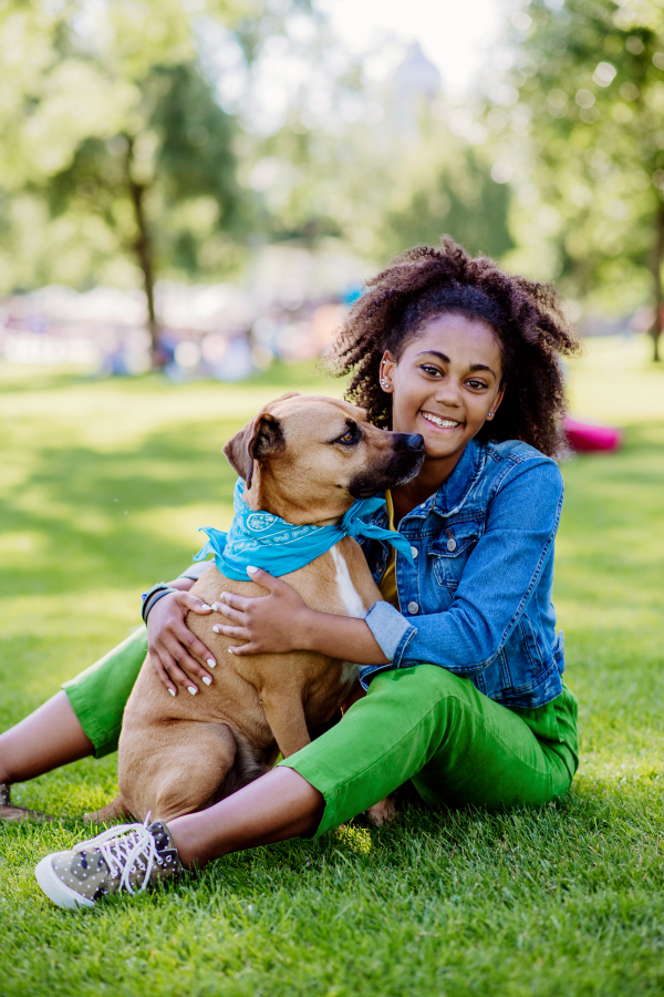 Multiracial girl sitting and resting with her dog outside in the park, training him, spending leisure time together. Concept of relationship between a dog and teenager, everyday life with pet.