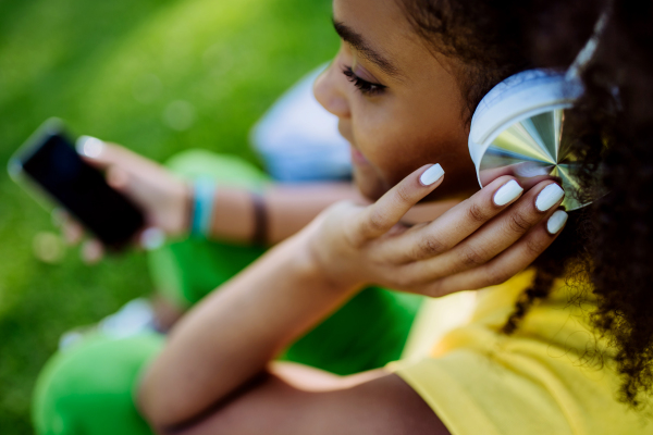 Multiracial girl sitting in a grass and enjoying music in headphones, high angle view.