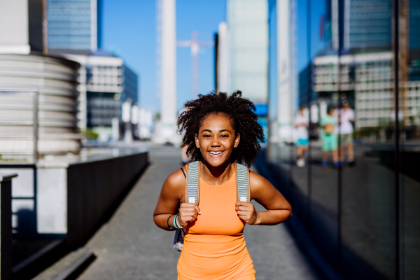 Multiracial teenage girl walking with a backpack in modern city centre during summer day, back to school concept.