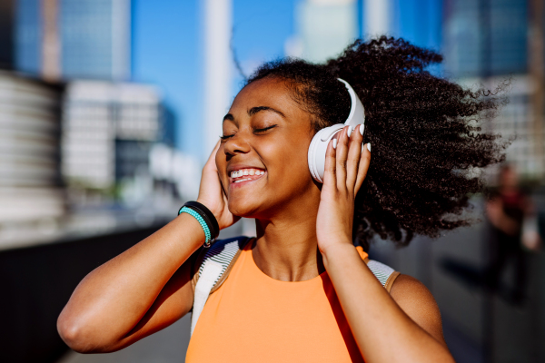 Multiracial girl enjoying music in headphones, during a city walk.