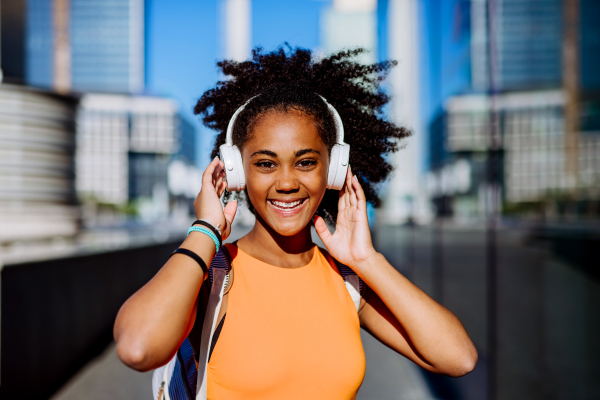 Multiracial girl enjoying music in headphones, during a city walk.