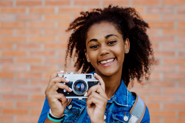 Multiracial girl standing in front of brick wall with a camera, and posing.