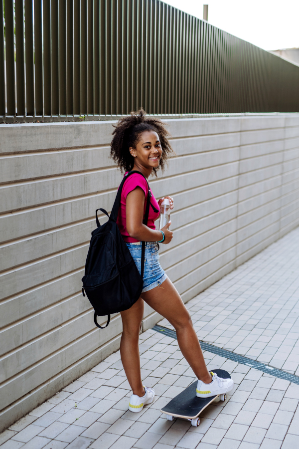 Multiracial teenage girl with backpack at skateboard, during a summer day.