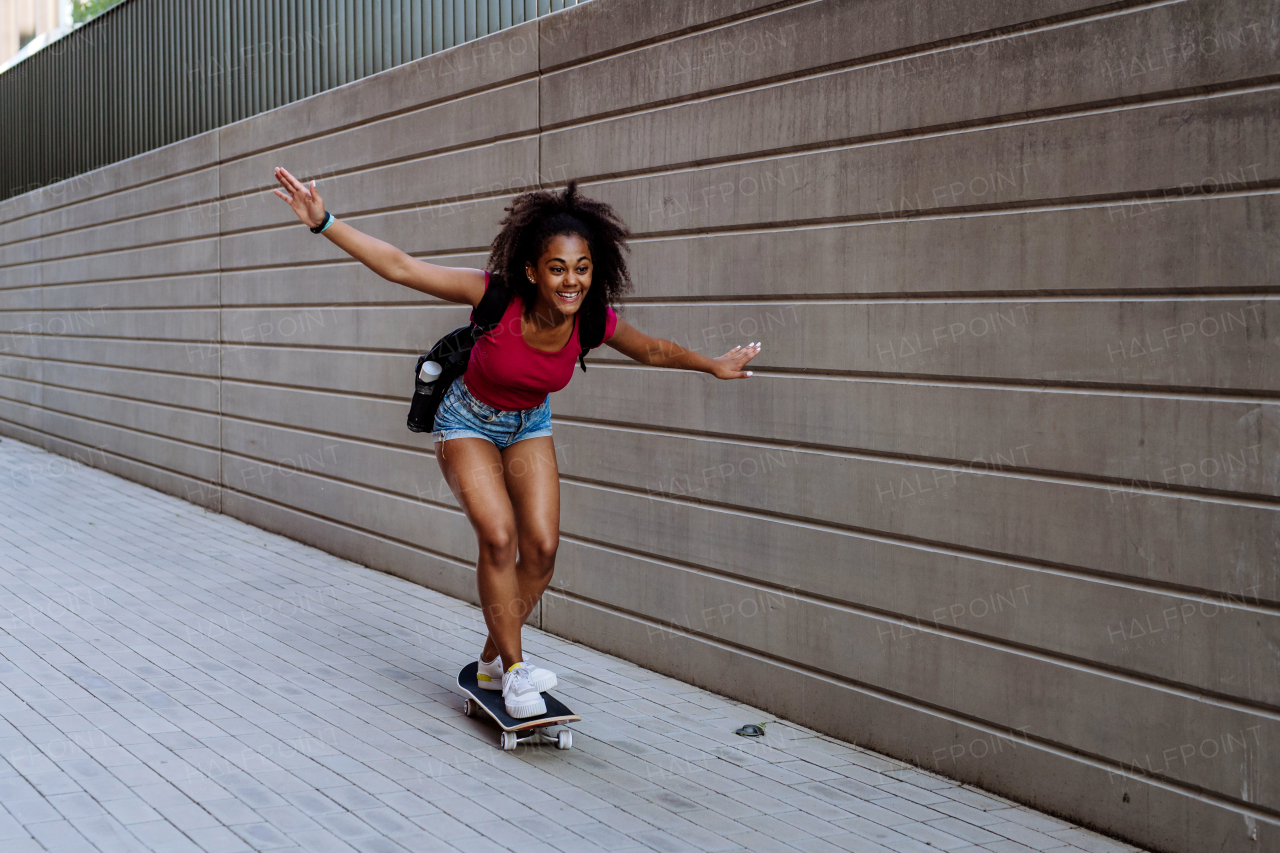 Multiracial teenage girl riding skateboard in front of concrete wall, balancing. Side view.