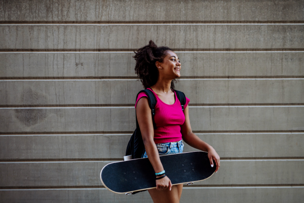 Multiracial teenage girl with a skateboard, walking in city during a summer day.