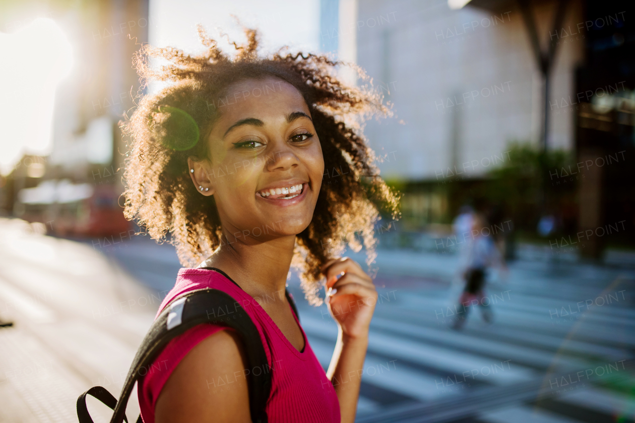 Multiracial teenage girl walking in modern city centre during summer sunset. Side view.