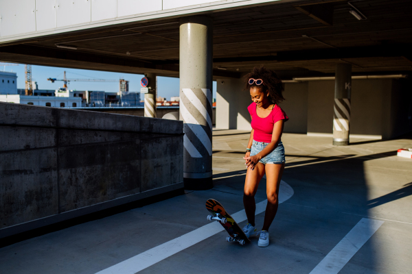 Multiracial teenage girl skateboarding in modern city during summer day.