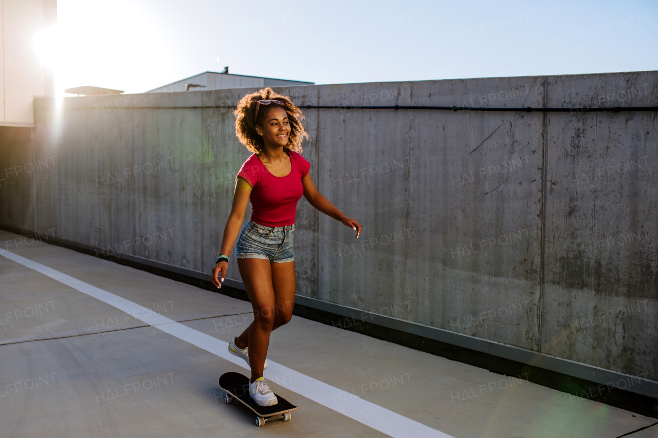 Multiracial teenage girl riding skateboard in front of concrete wall, balancing. Side view.