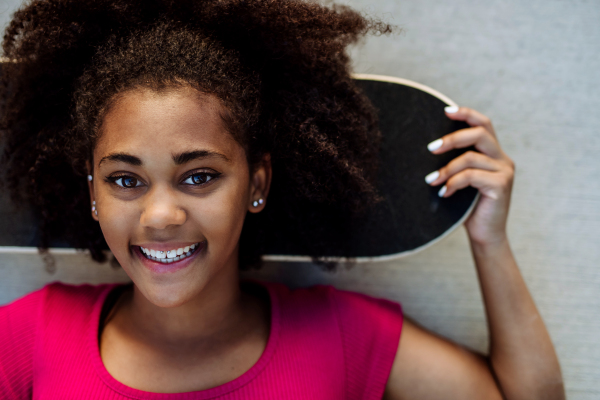 Multiracial teenage girl with skateboard, in front of concrete wall during summer day.