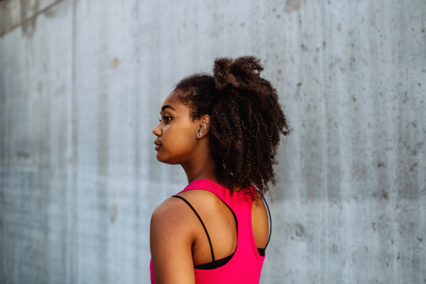 Rear view of young mulitiracial girl standing in front of a city concrete wall.