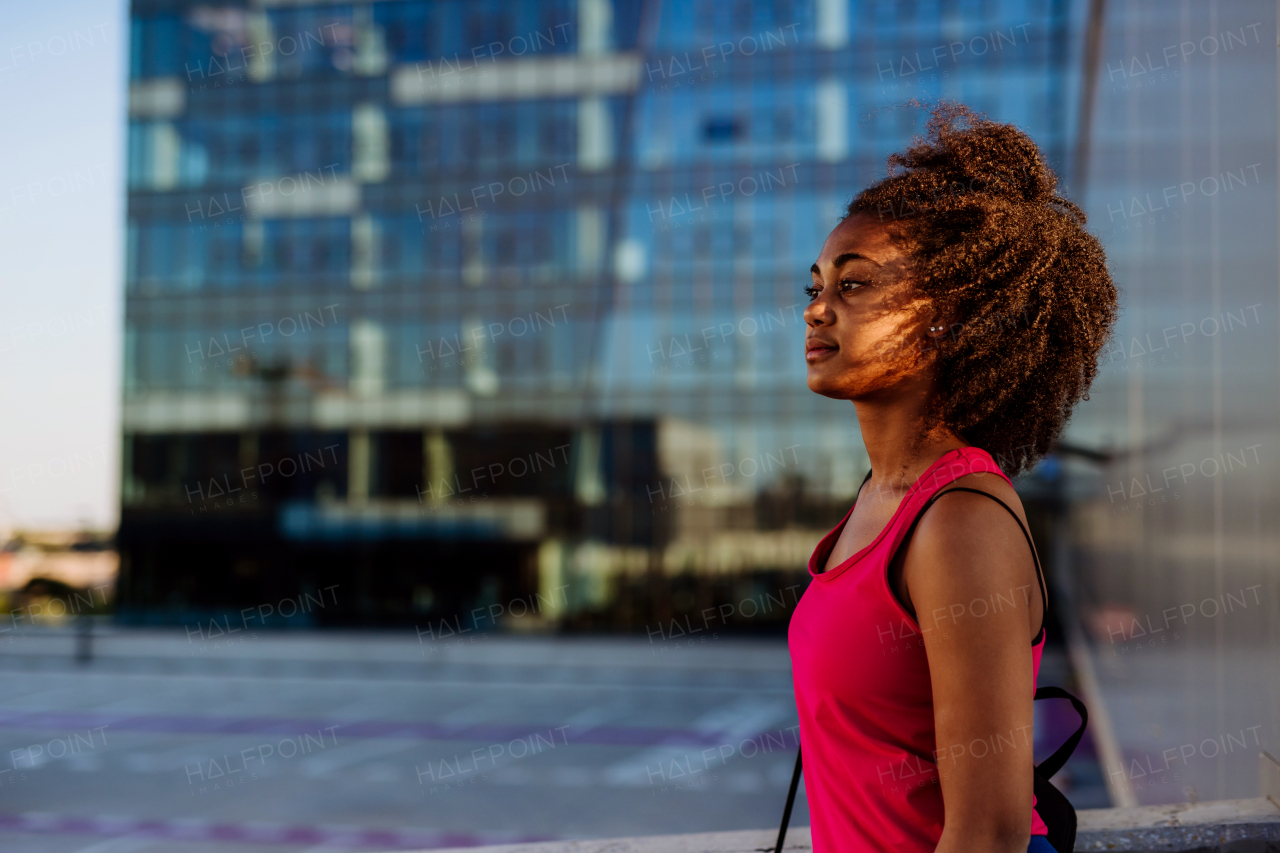 Multiracial teenage girl walking in modern city centre during summer sunset. Side view.