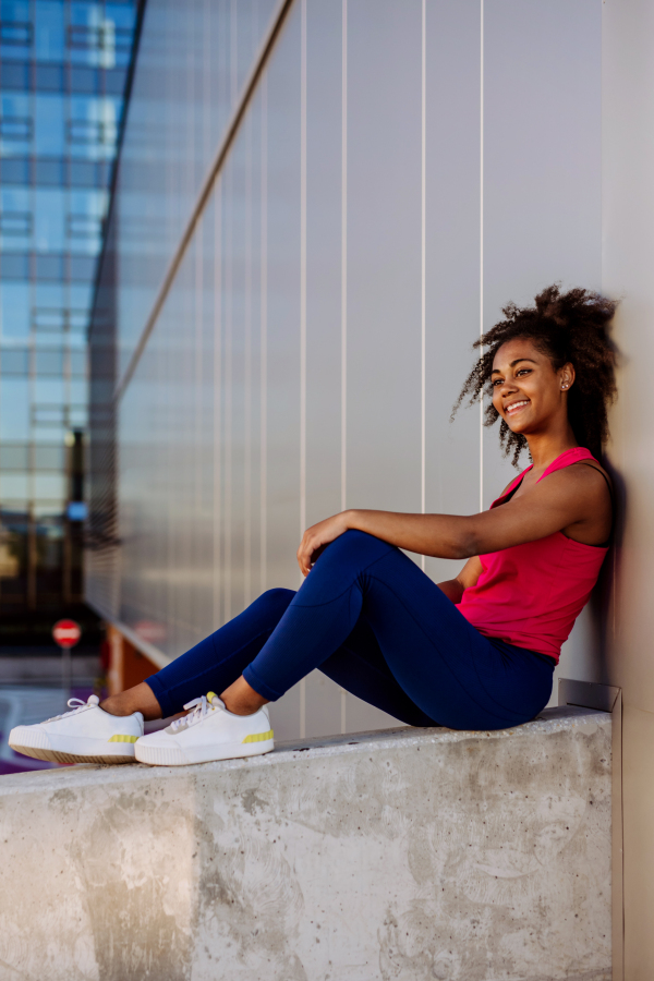 Young multiracial girl in sportswear resting and sitting after jogging in a city.