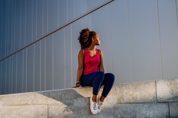 Young multiracial girl in sportswear resting and sitting after jogging in a city.