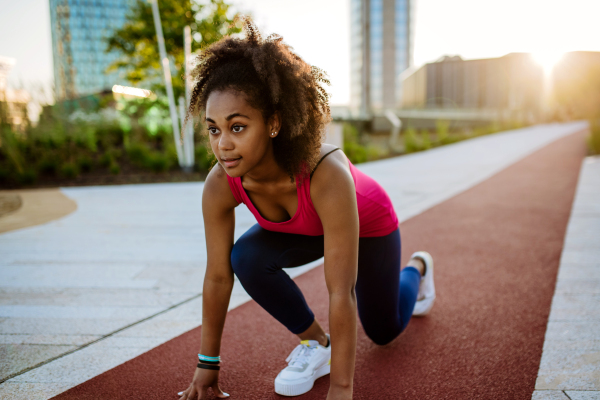 Young multiracial girl in sportswear preparing for run in a city, during summer sunset, golden hour.