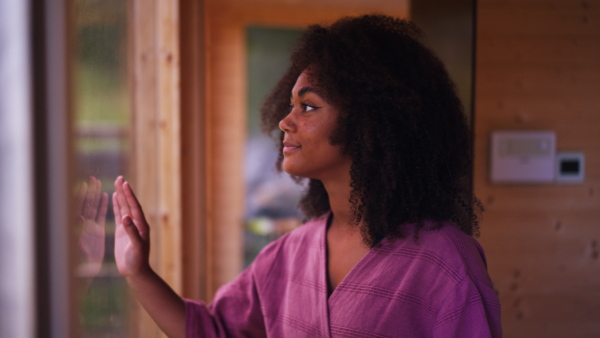 A peaceful morning for young woman standing on balcony in bathrobe, looking at beautiful nature around her, smiling.