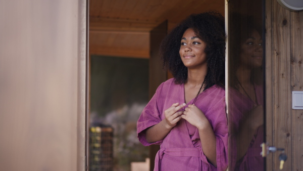 A peaceful morning for young woman standing on balcony in bathrobe, looking at beautiful nature around her, smiling.