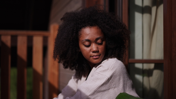 A peaceful morning for young woman sitting on balcony in bathrobe, looking at beautiful nature around her, smiling.