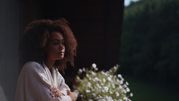 A peaceful morning for young woman standing on balcony in bathrobe, looking at beautiful nature around her, smiling.