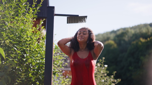 A beautiful young woman taking shower outdoors, in the middle of nature and lush foliage. Outdoor shower in garden.