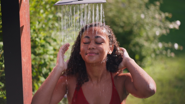 A beautiful young woman taking shower outdoors, in the middle of nature and lush foliage. Outdoor shower in garden.