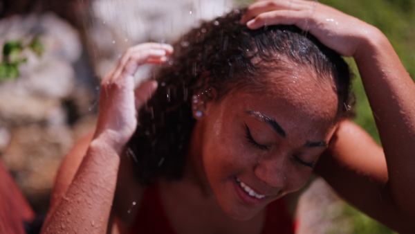 A beautiful young woman taking shower outdoors, in the middle of nature and lush foliage. Outdoor shower in garden.