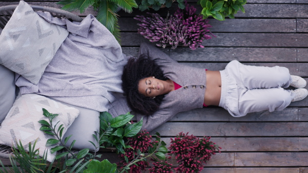 A young woman lying on patio with closed eyes having peaceful moment. Beautiful african american woman resting, in connection with plants around her.