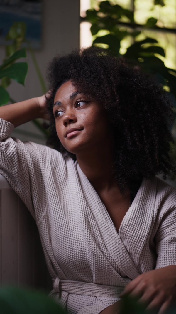 A pensive woman sitting by bathtub, lush indoor plants around her. Woman getting ready for bath, enjoying peaceful morning moment alone