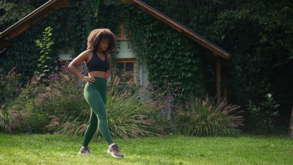 A young woman exercising outdoors on lawn in the garden. Beautiful african american woman connecting with herself and nature.