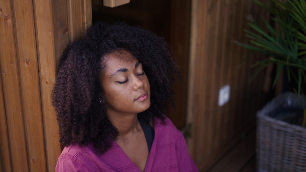 A peaceful morning for young woman sitting outdoor in the garden in bathrobe, doing breathing exercises with closed eyes.