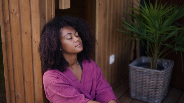 A peaceful morning for young woman sitting outdoor in the garden in bathrobe, doing breathing exercises with closed eyes.