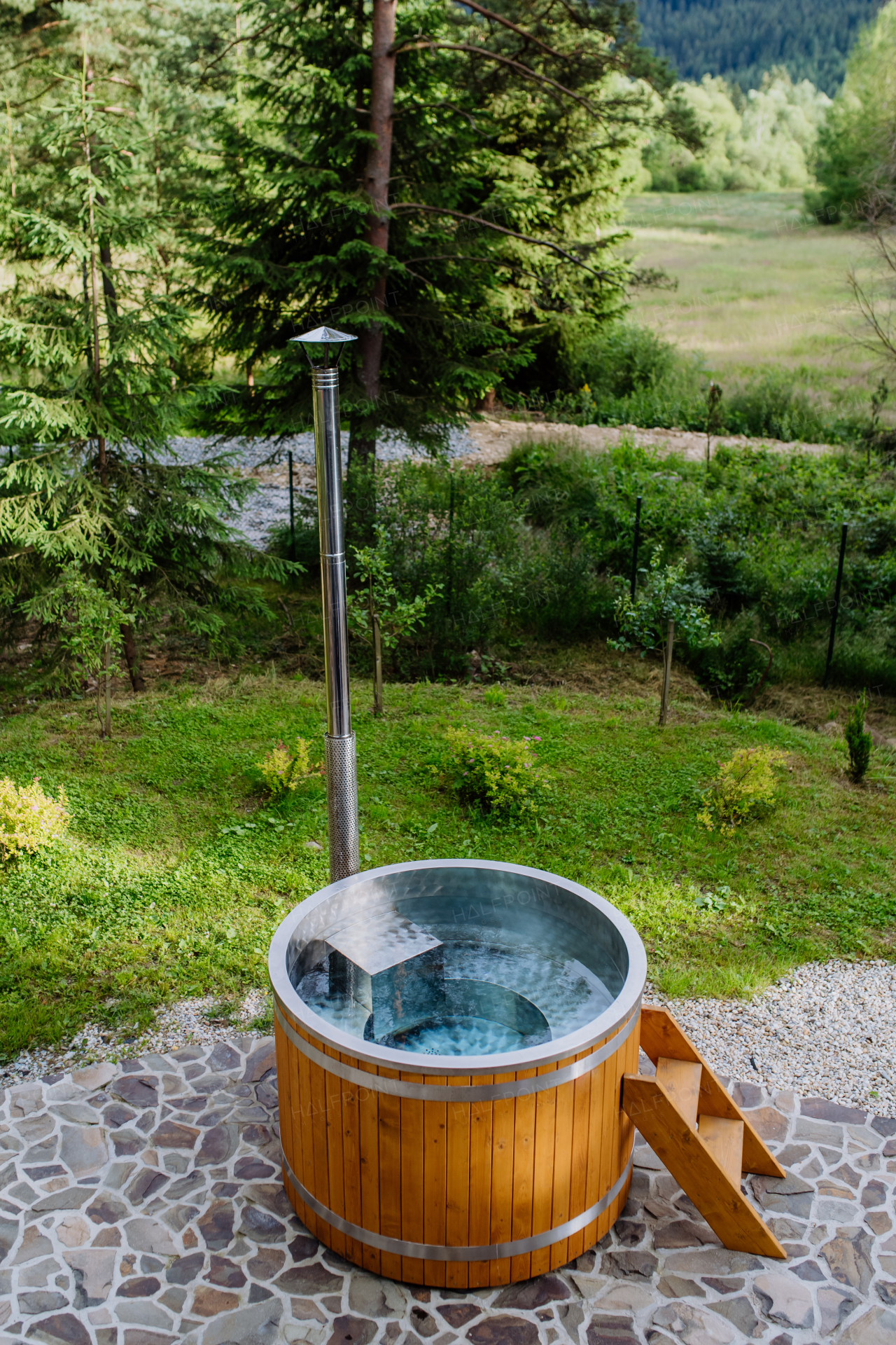 A wooden bathtub with a fireplace to burn wood and heat water in backyard in mountains.