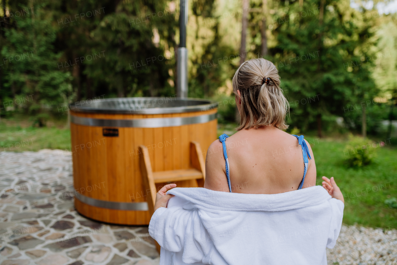 A young woman preapring to get into hot bath outdoors. Summer holidays in the mountains, hot water treatments and thermal spa concept, rear view.