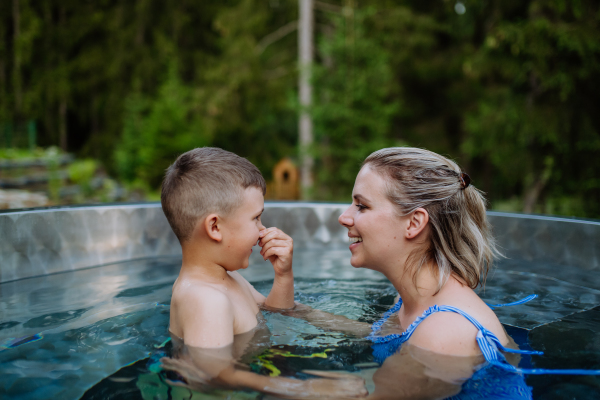 A other with her little son enjoying bathing in wooden hot tub in the terrace of the cottage.