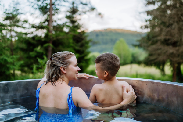 A mother with her little son enjoying bathing in wooden barrel hot tub in the mountains.