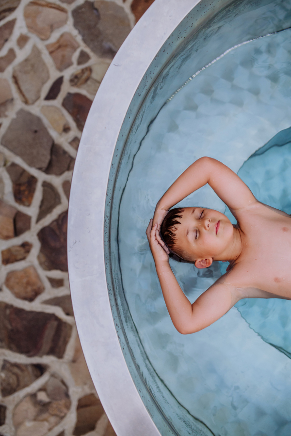 A top view of little boy relaxing with eyes closed in hot tub. Summer holiday, vacation concept.