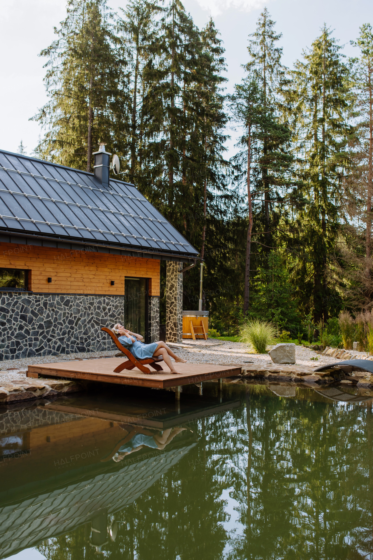 A rlaxed woman wearing headphones listening to music lying on a pier by natureal lake in summer