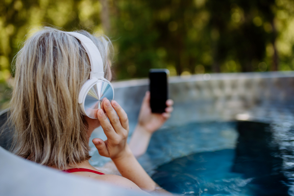 Reaxed woman with a headphones listening to music in outdoor bathtub, rear view.