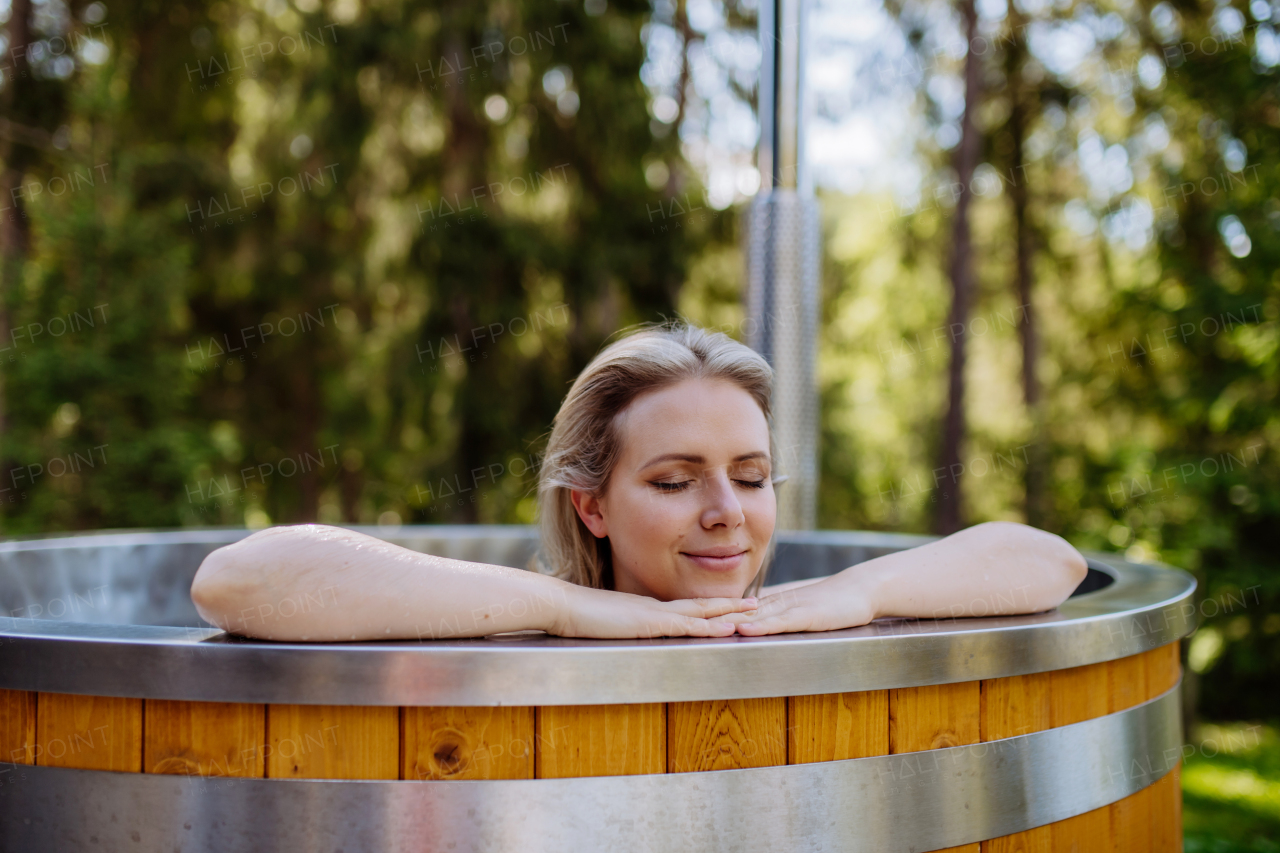 Young woman enjoying wooden bathtub with fireplace to burn wood and heat water in backyard in mountains.