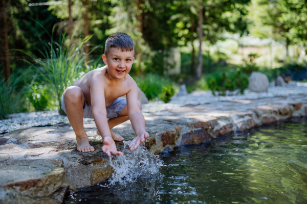 Little boy coming out from garden pond with splashing around him. Summer holiday, vacation concept.