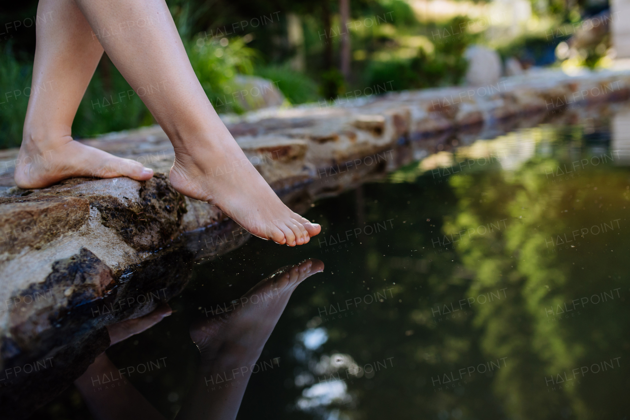 An unrecognizable young woman is dipping her foot in cool water of pond, refreshing and hardening concept.