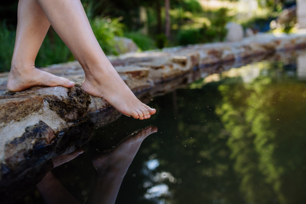 An unrecognizable young woman is dipping her foot in cool water of pond, refreshing and hardening concept.