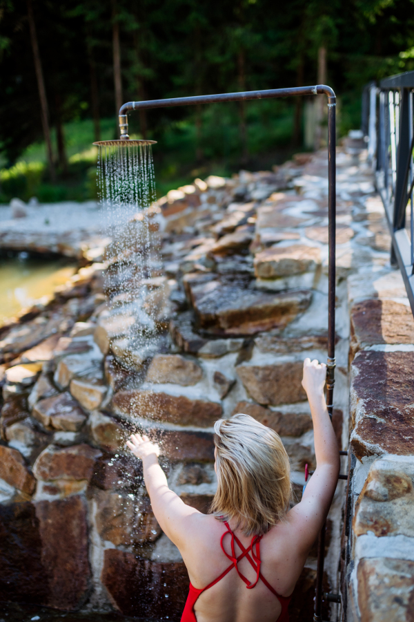 A rear view of woman in swimsuit taking bath in outdoor shower in garden