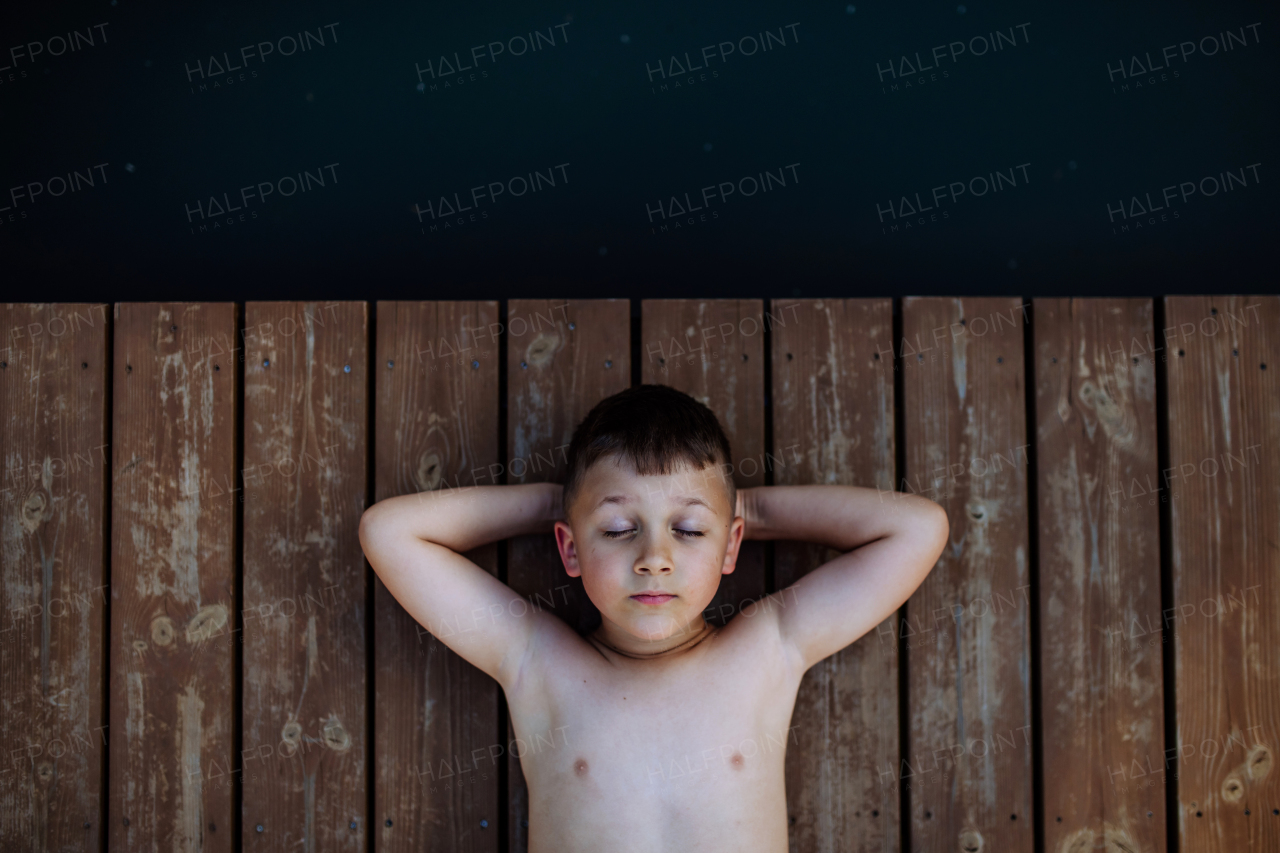 A little boy relaxing with eyes closed in on pier by lake. Summer holiday, vacation concept.