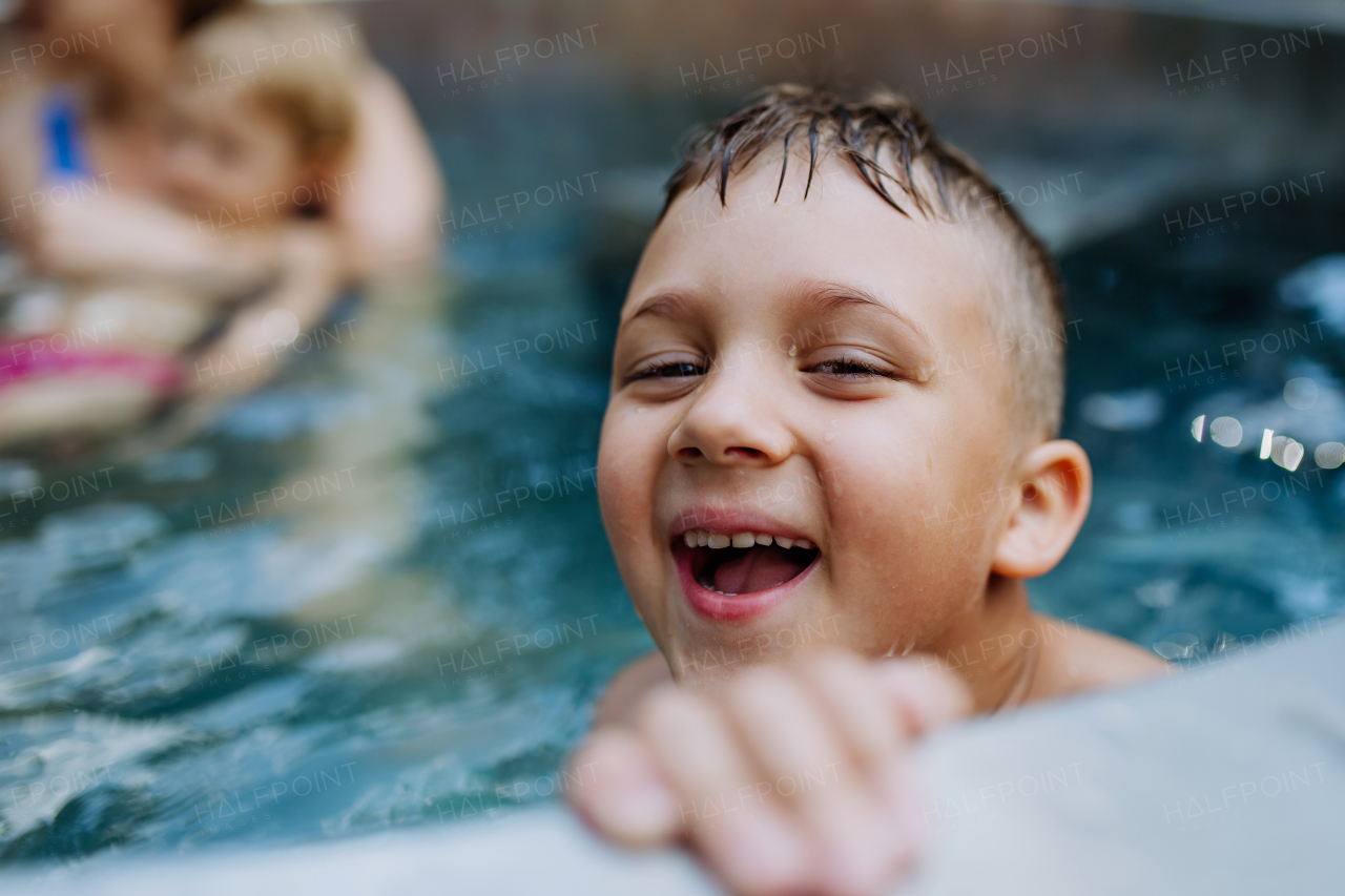 Little boy enjoying summer time in the outdoor pool with his family, having fun.