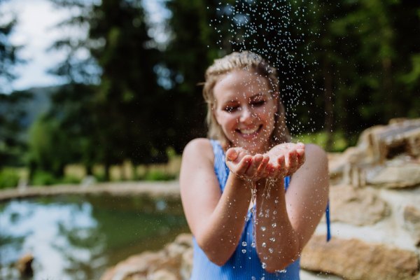 Happy young woman resting and enjoying water in a swimsuit near lake, during hot sunny day on summer vacation.