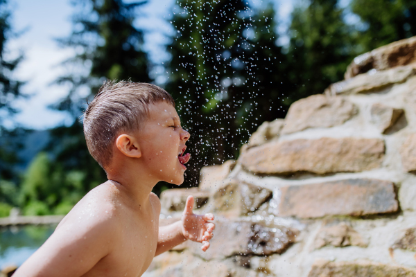 Little boy coming out from garden pond with splashing around him. Summer holiday, vacation concept.